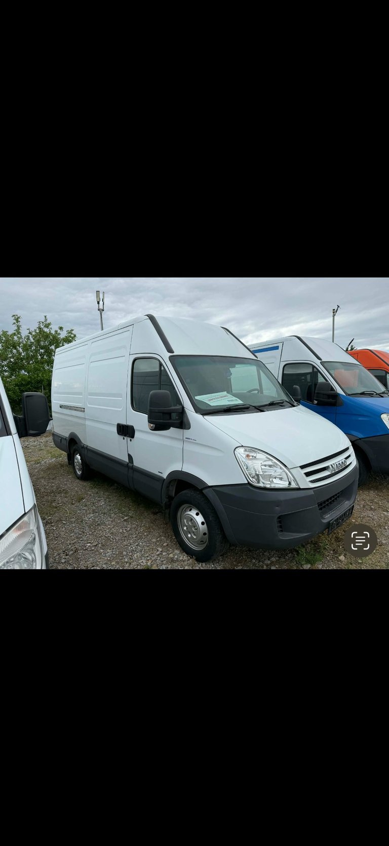 White Iveco commercial van parked in a lot with other vehicles and cloudy sky in background