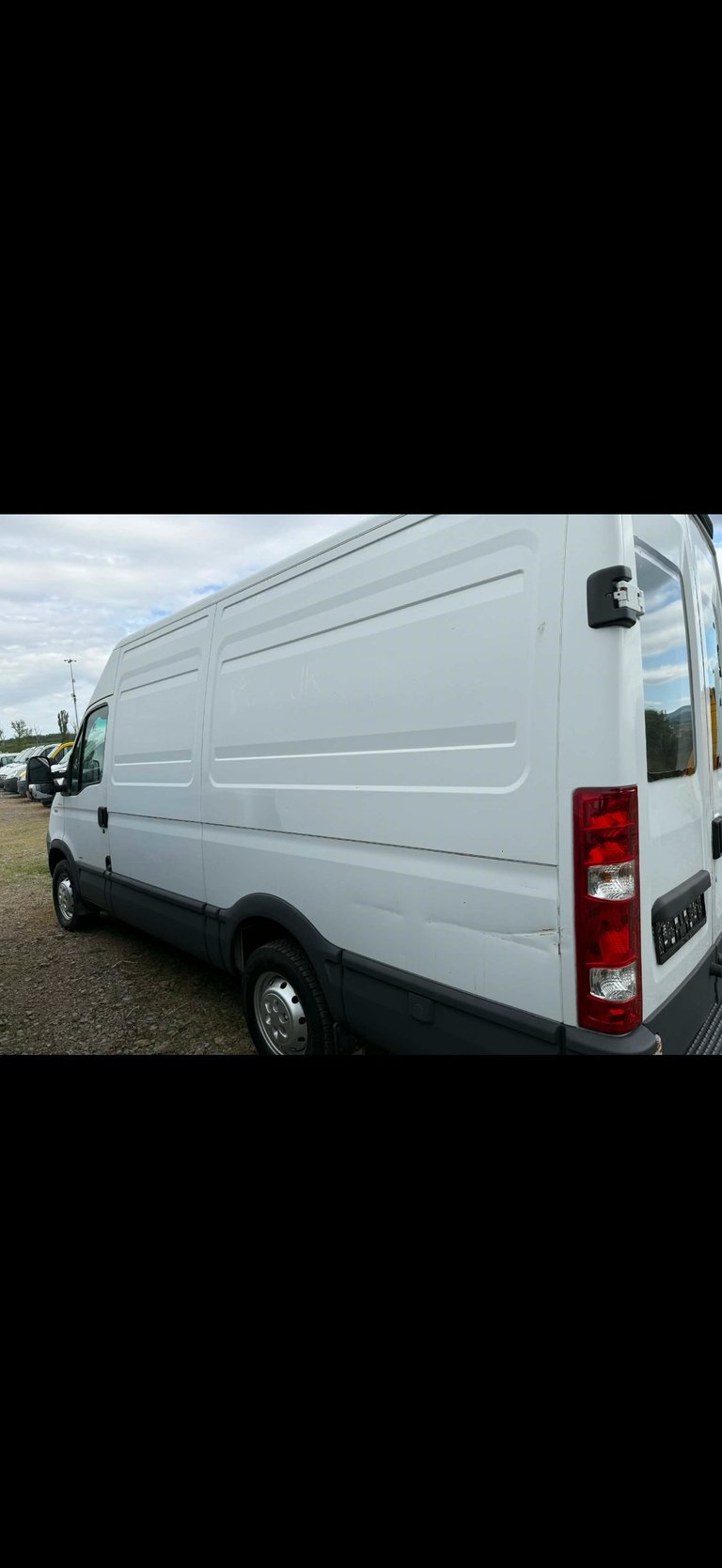 White commercial delivery van parked outdoors, showing rear and side view with red taillights