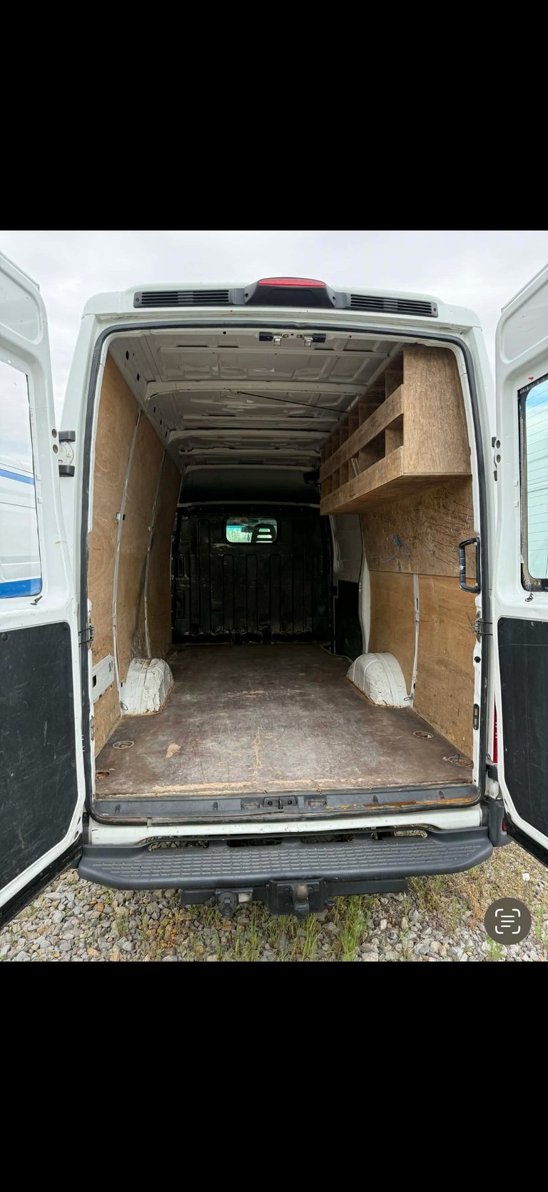 Interior of white commercial delivery van with open rear doors showing empty cargo space with plywood walls and metal floor